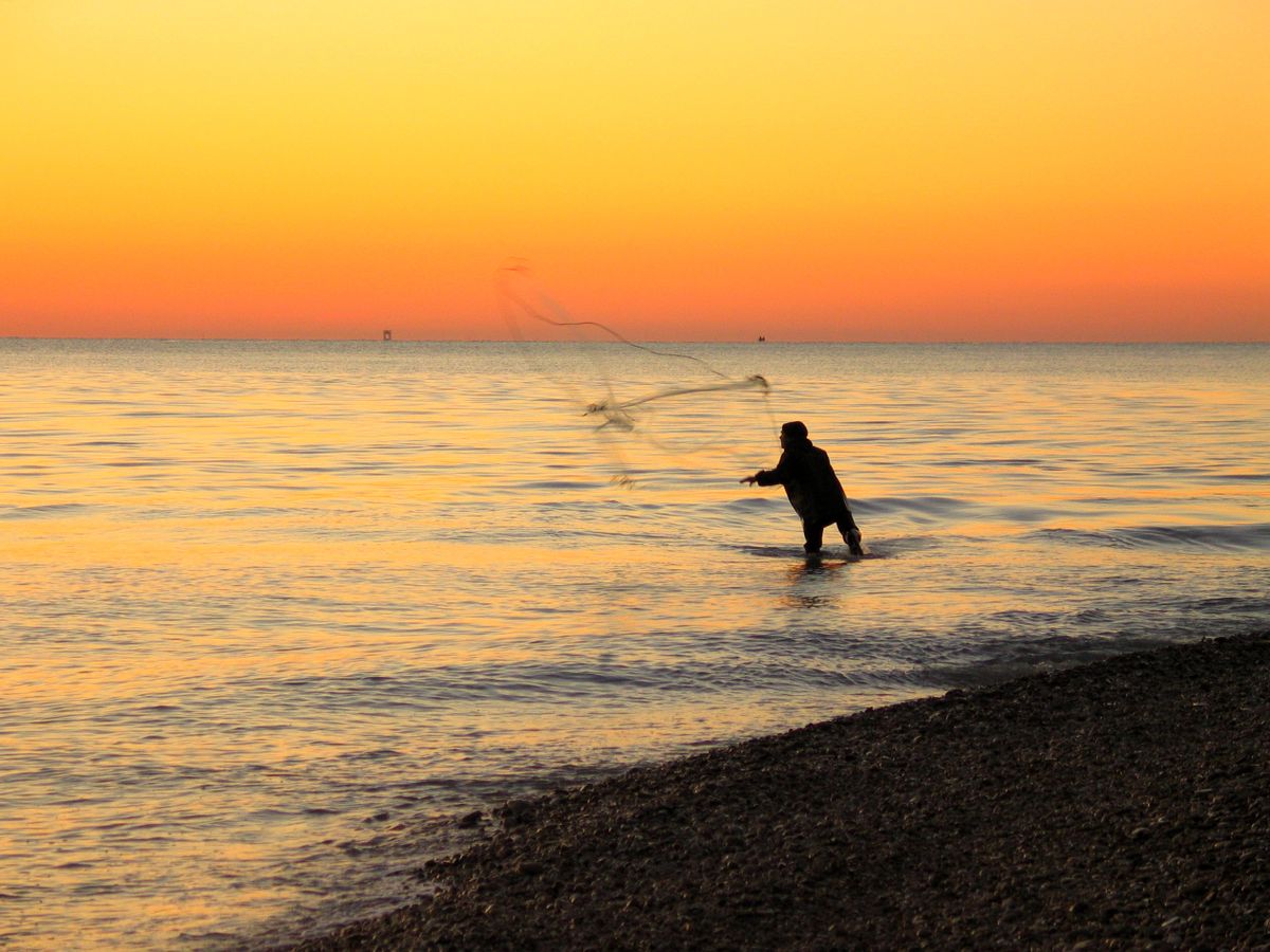 A fisherman casting a net from the Adriatic shore at sunset